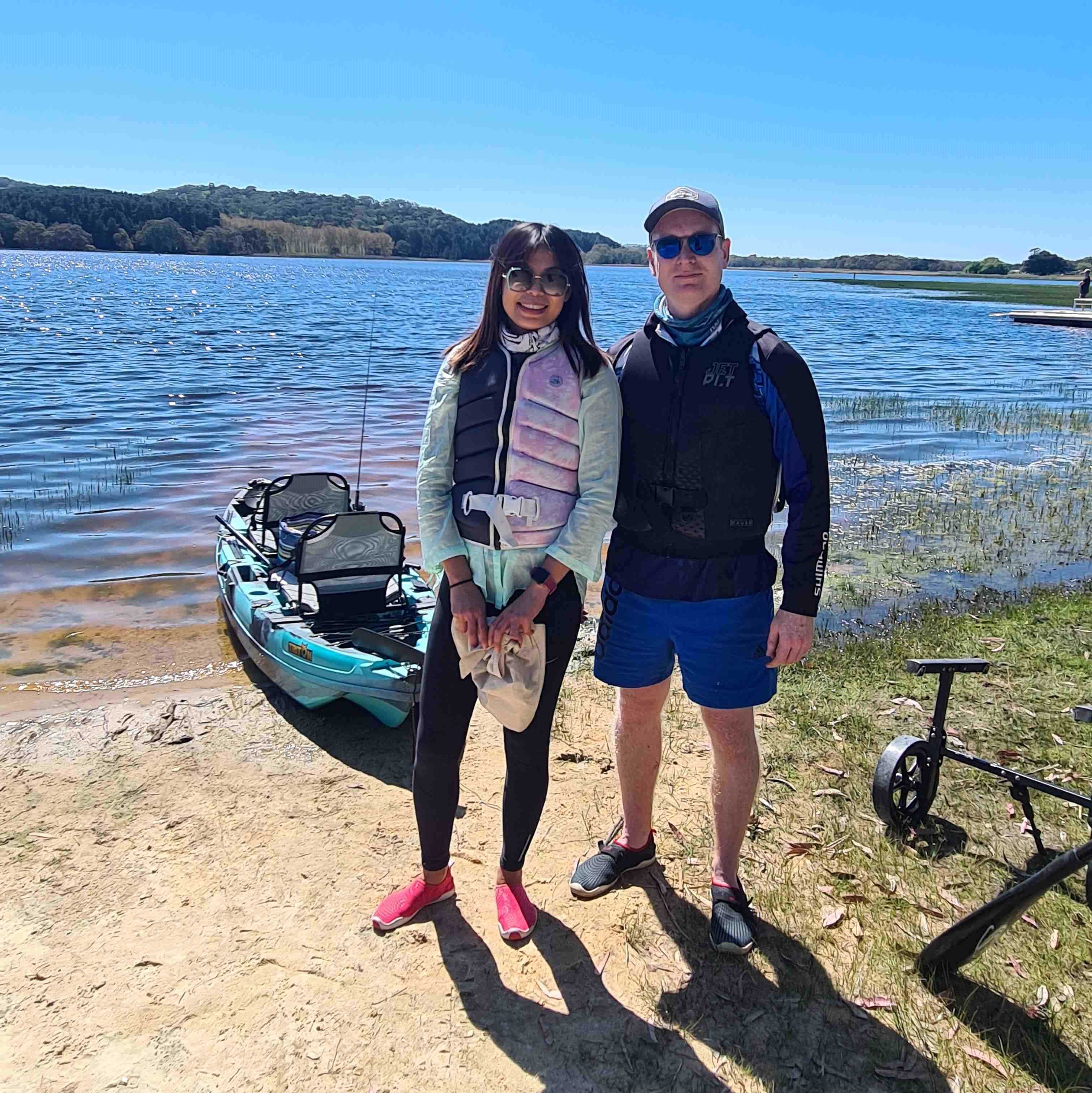 Tow people standing in front of a kayak on the banks of the Myponga Reservoir wearing lifejackets