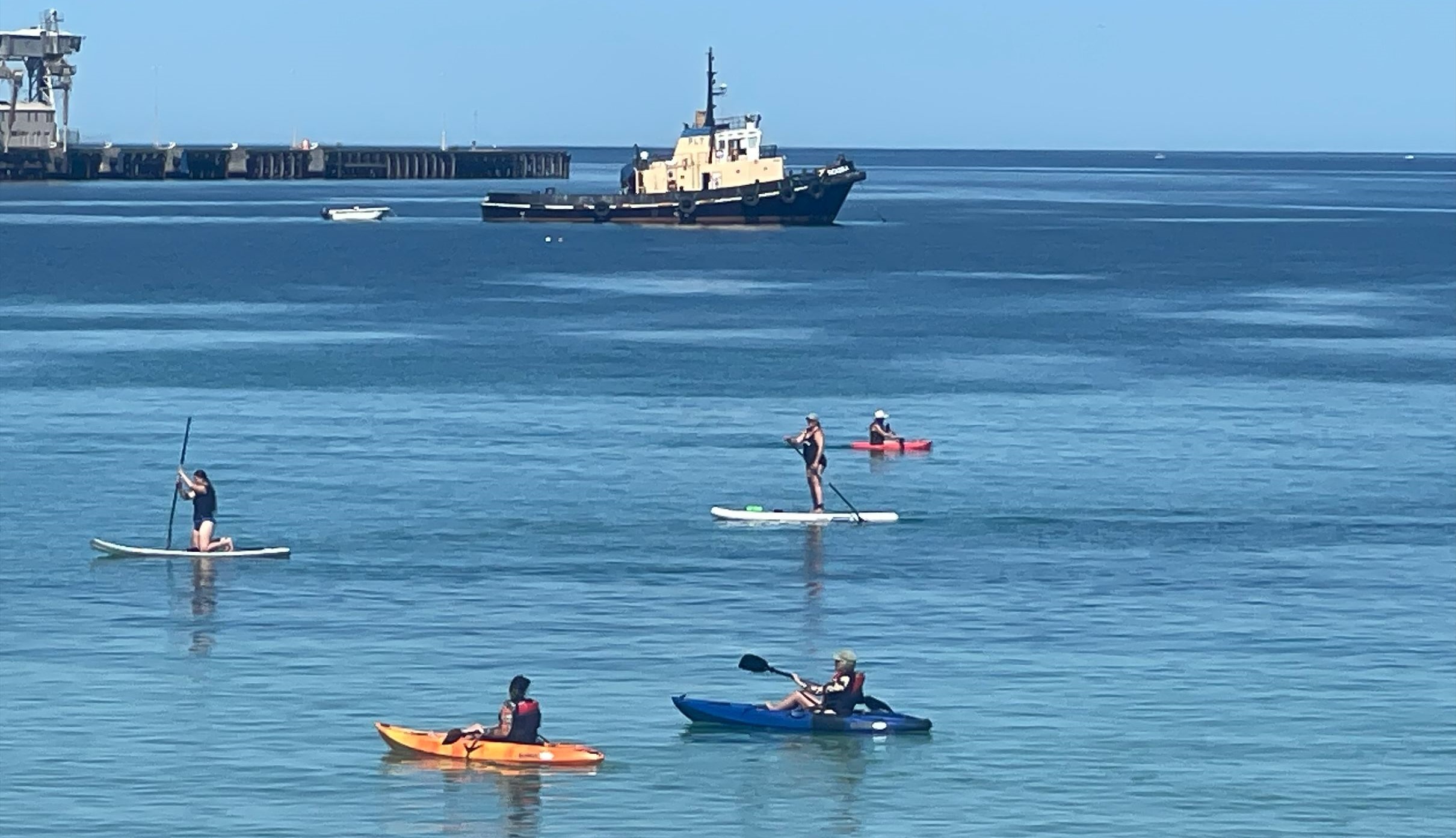 5 people on unpowered craft on water at Wallaroo with a tug boat and boat in the background