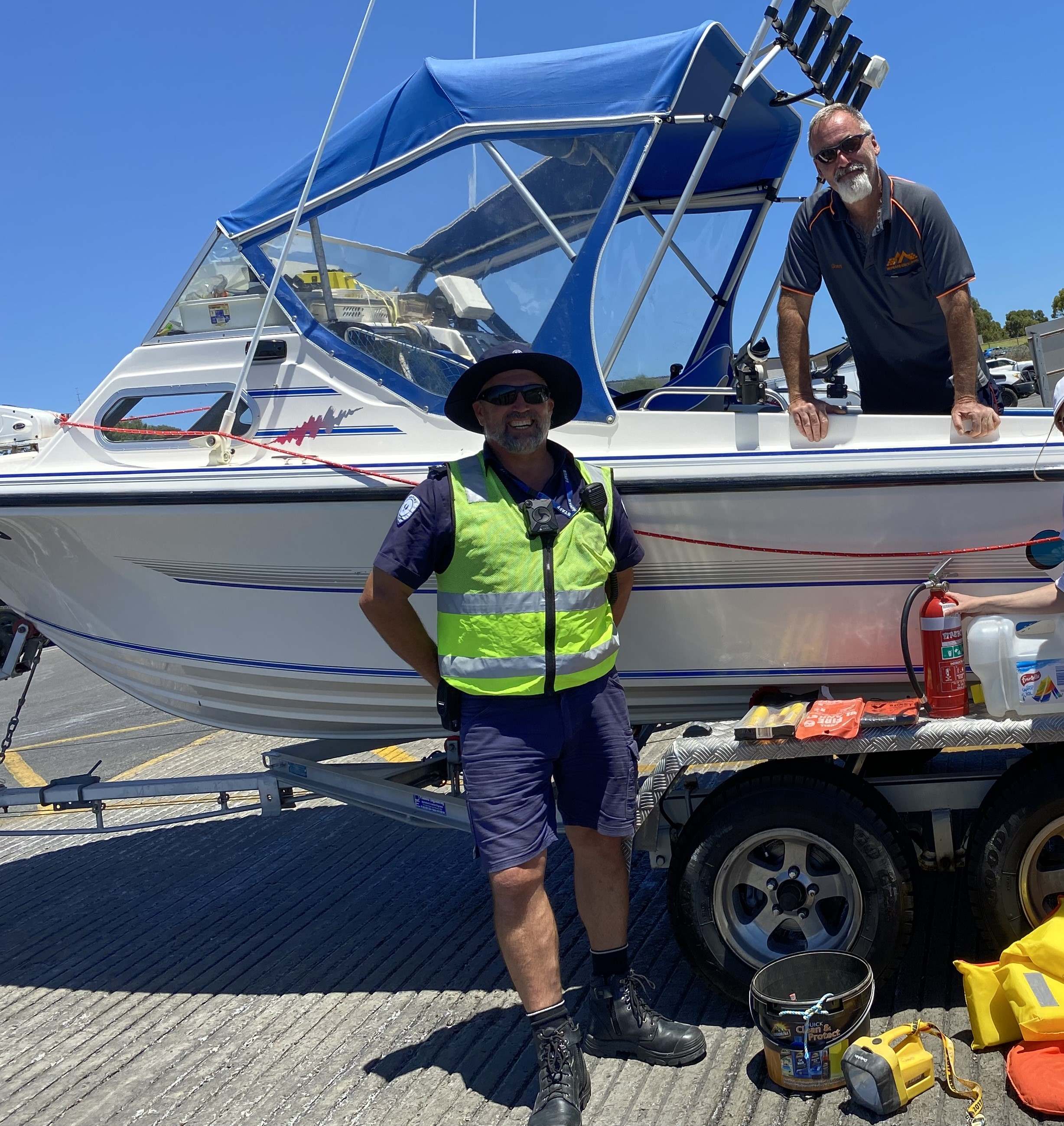 Marine Safety Officer in front of a boat at a boat ramp with a boater in the boat with safety equipment lying on the ground