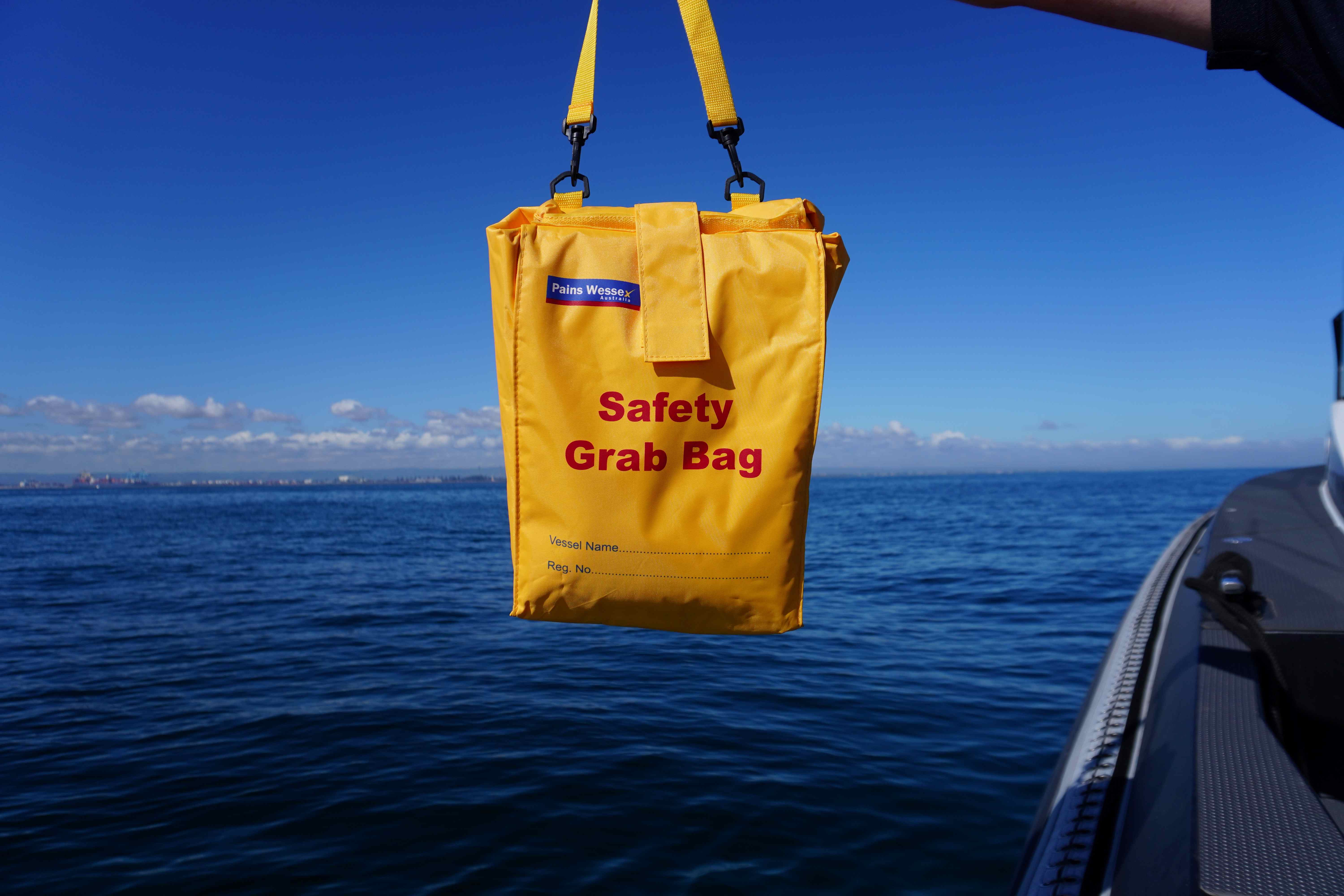 In this image is a photo of a safety grab bag which should have most of your safety equipment that you require on board your vessel. Grab bag is yellow and background is the blue ocean and blue sky